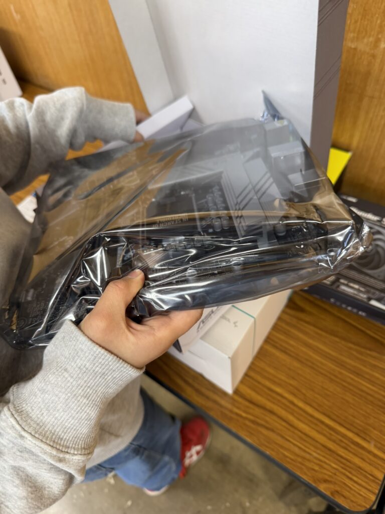 "子どもがマザーボードを静電気防止袋から取り出している手元"